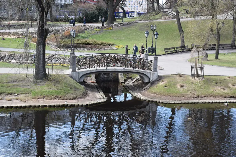 The City Canal running through Bastejkalns park in Riga, with a small arched stone footbridge and manicured lawns