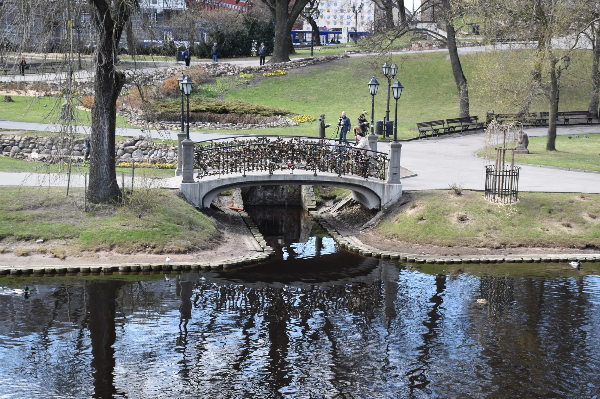 The City Canal running through Bastejkalns park in Riga, with a small arched stone footbridge and manicured lawns