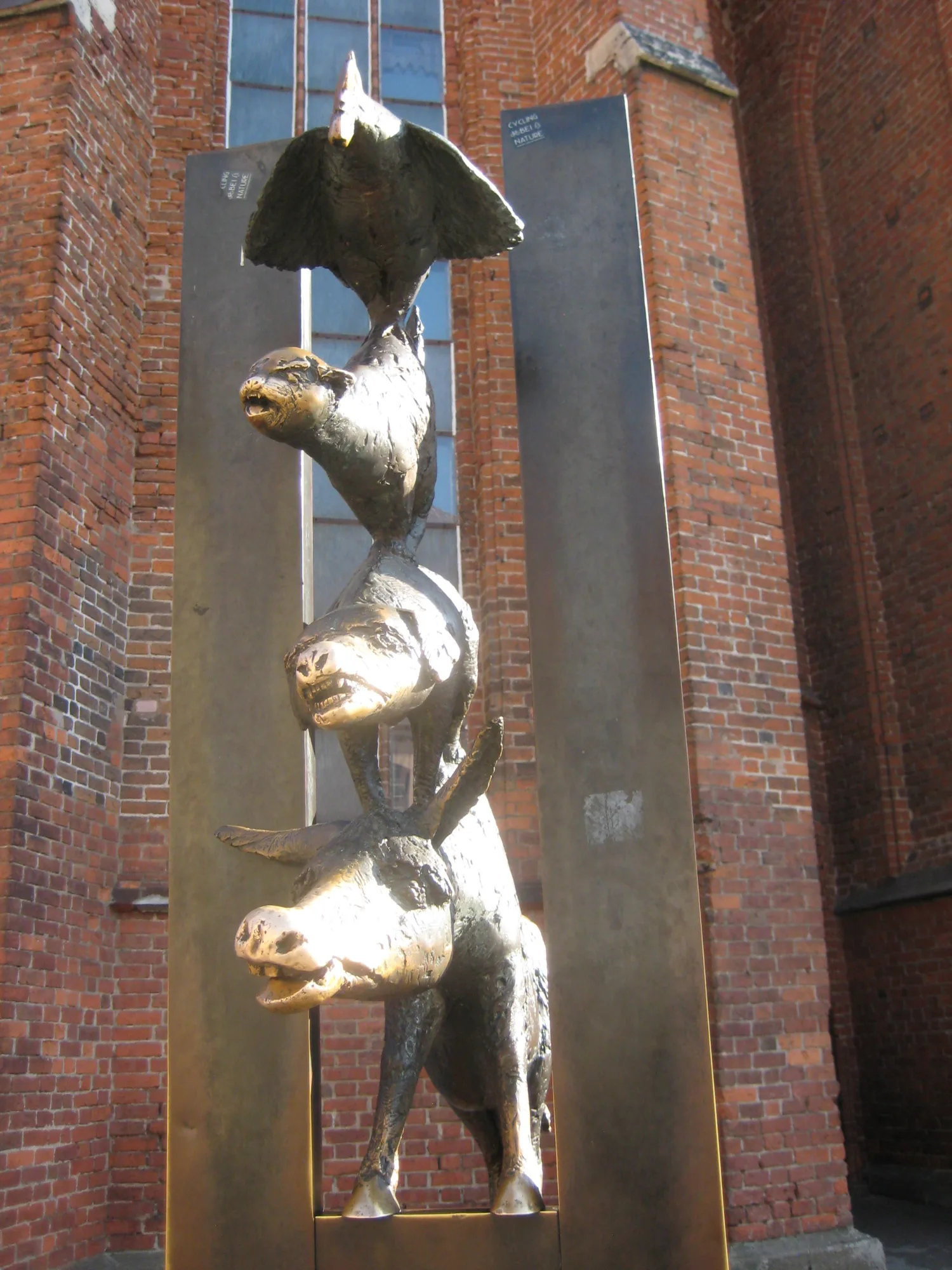The bronze Bremen Town Musicians statue in Riga: a donkey, dog, cat and rooster stacked and peering through a gap