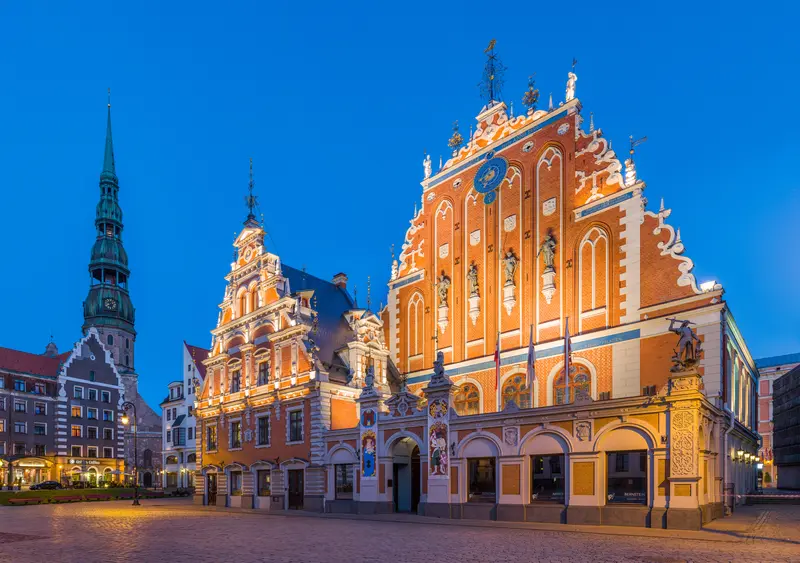 The ornate red Dutch-Renaissance gable of the House of the Blackheads on Town Hall Square in Riga, with St. Peter's spire behind