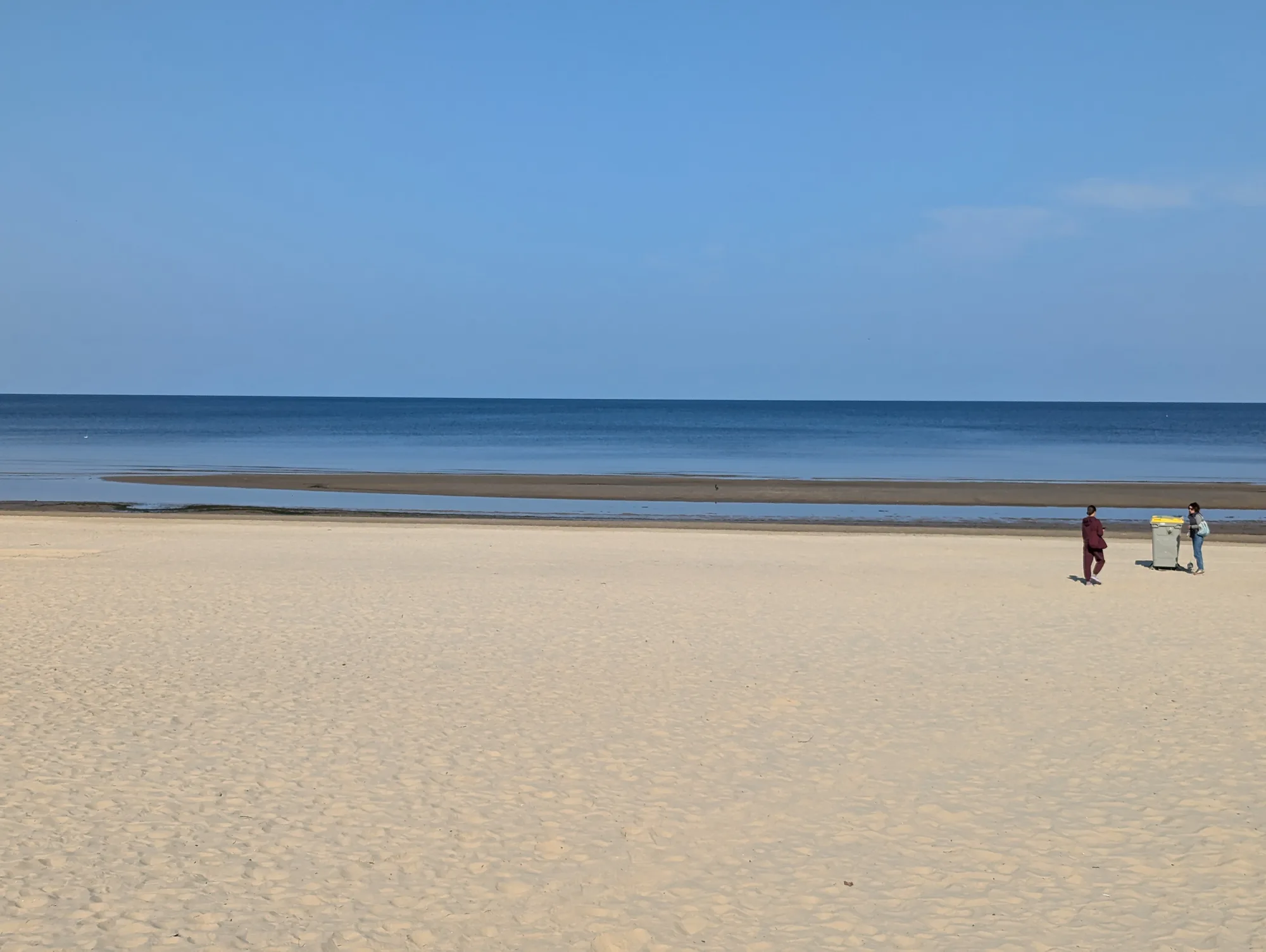 The wide flat pale-sand Baltic beach at Dzintari in Jurmala, with calm sea and a low forested shoreline