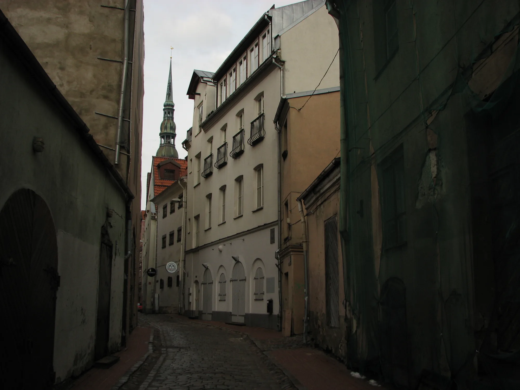A narrow cobblestone lane in Riga's Old Town lined with historic gabled houses, St. Peter's spire at the end