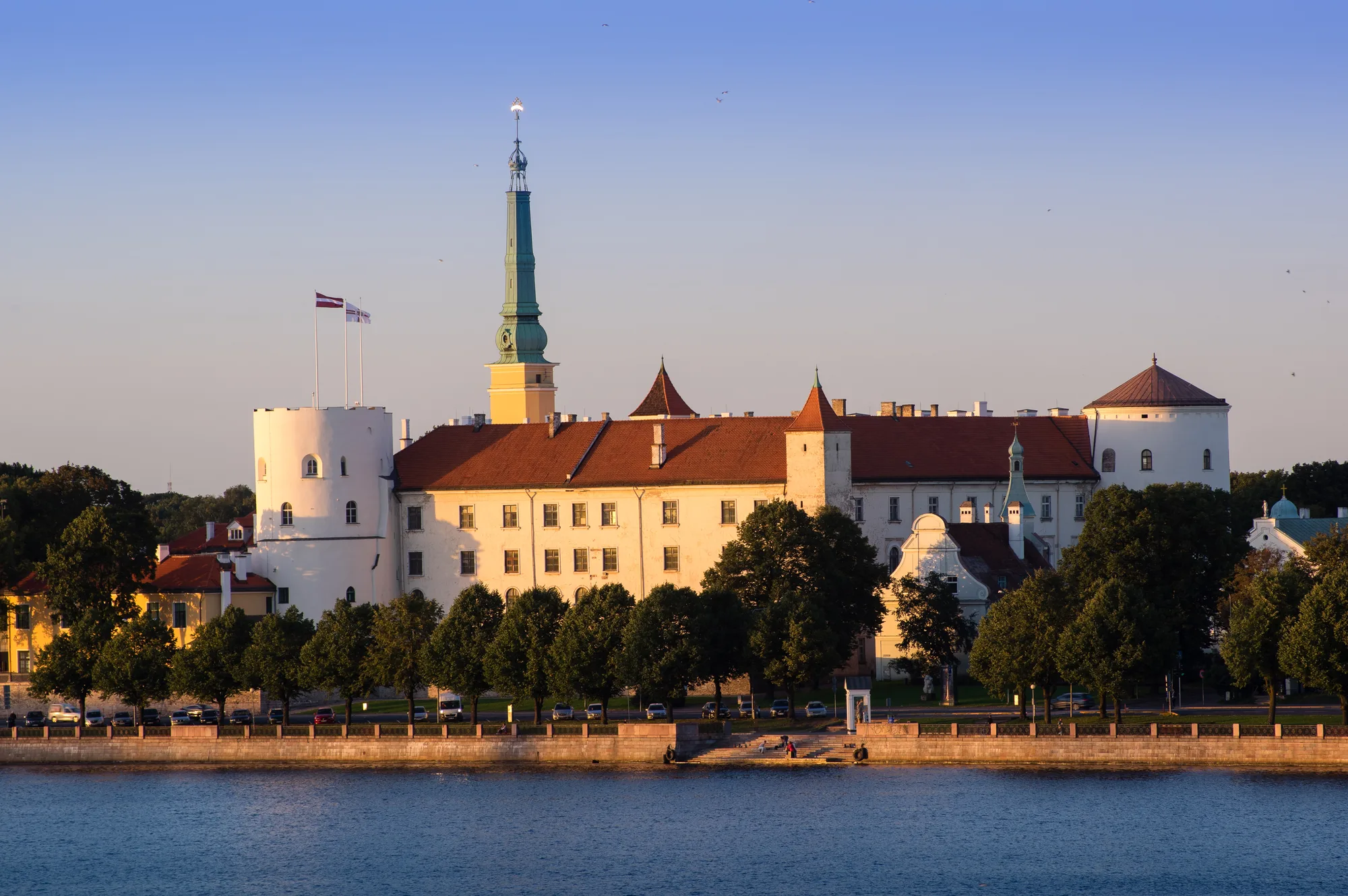 Riga Castle, a pale fortress with a round tower flying the Latvian flag, on the bank of the Daugava river