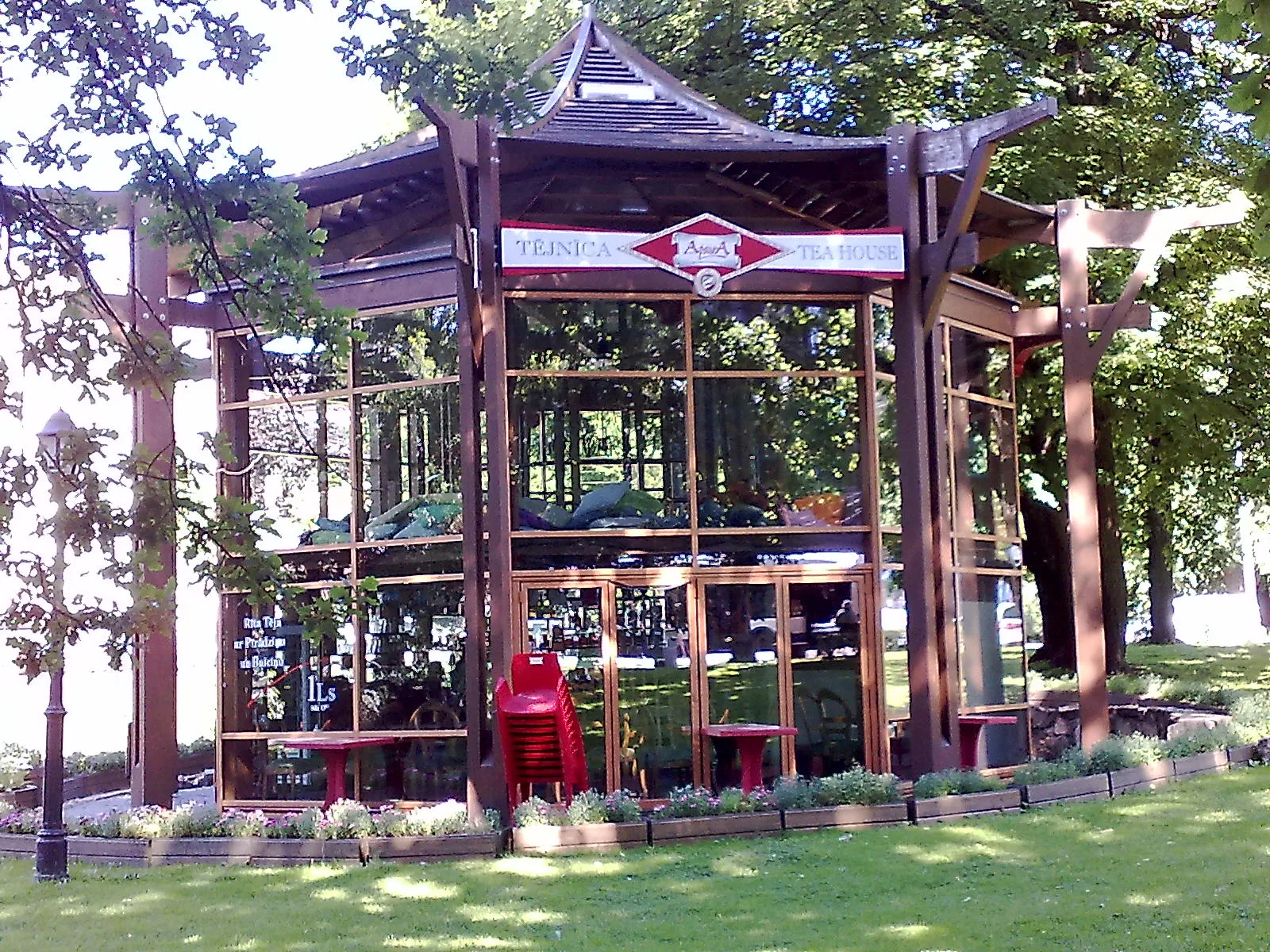 The glass-walled Tējas namiņš tea house, a wooden pavilion café set among trees beside the City Canal in central Riga